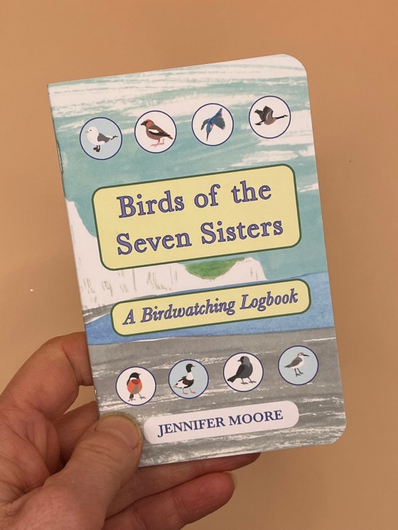Birds of the Seven Sisters Logbook being held in front of a sandy-coloured background